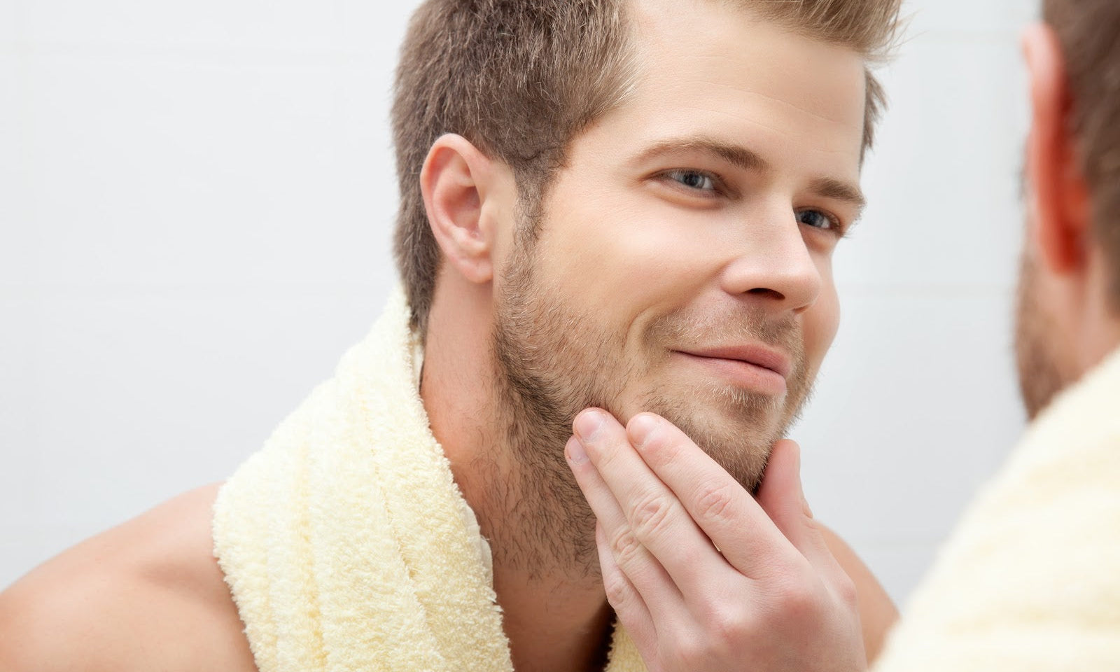 A man leaning toward a bathroom mirror, closely examining his cheeks and jawline