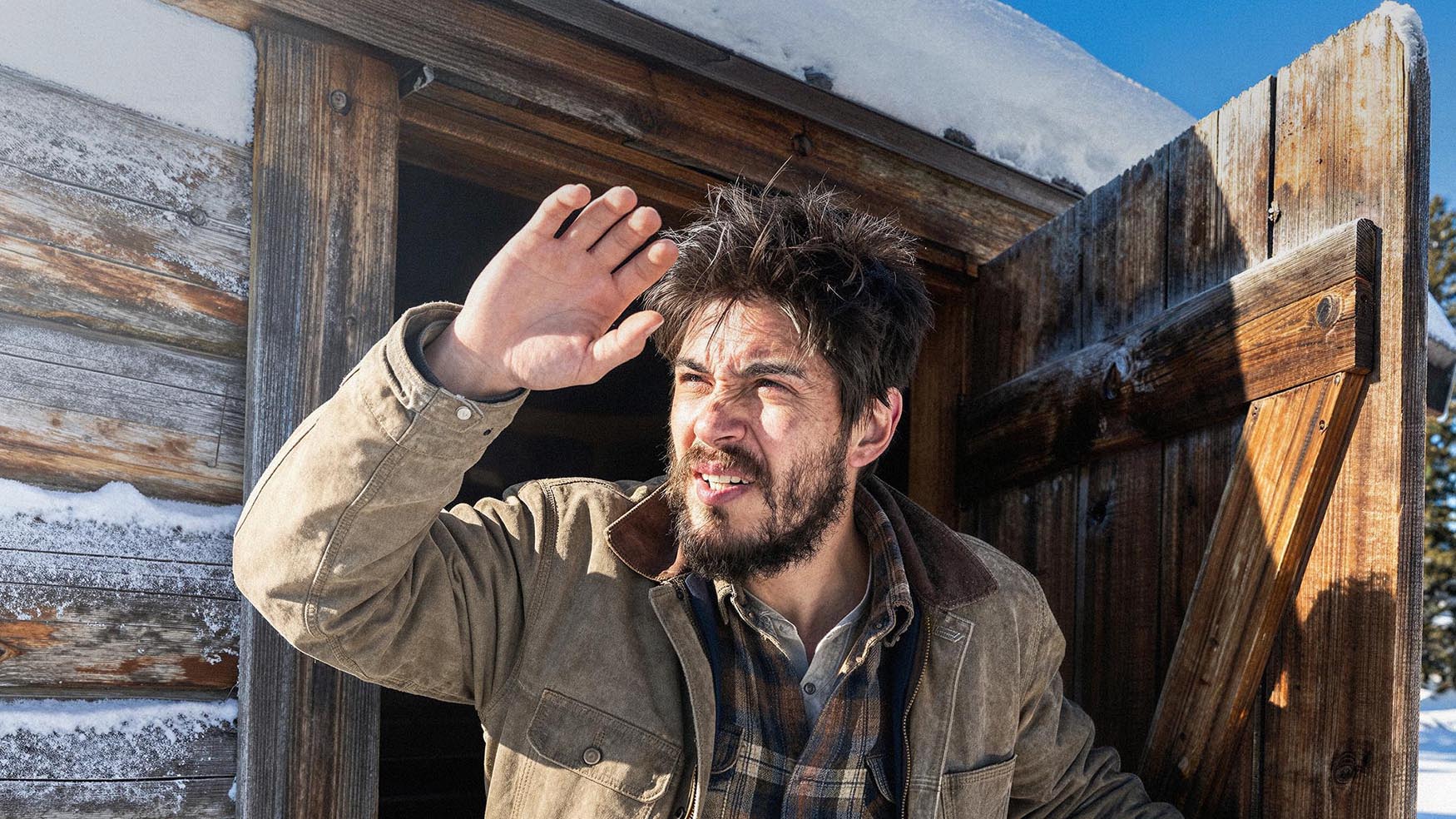 Bearded man standing outside a wooden cabin in a snowy winter landscape